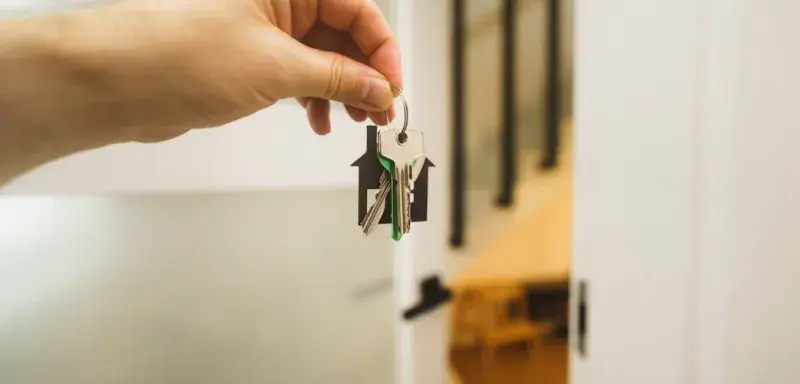 Une main tenant une clé devant une porte de maison