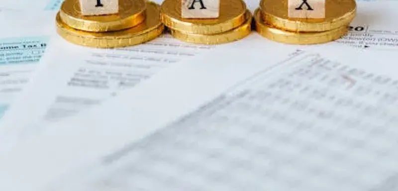 Pièces de monnaie dorées posées sur des documents fiscaux avec des lettres formant le mot taxe