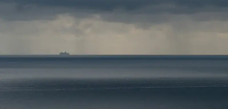 Un navire solitaire navigue sous des nuages orageux sur une mer vaste et menaçante