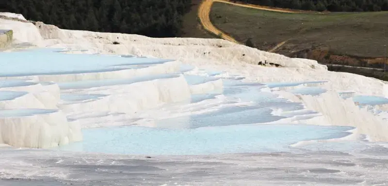 Terrasses naturelles de travertin avec eau bleue thermale au milieu des montagnes