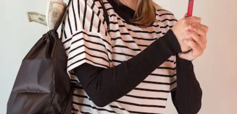 Une femme portant un masque de voleur et un bonnet, tenant un pied-de-biche et un sac avec de l'argent qui dépasse