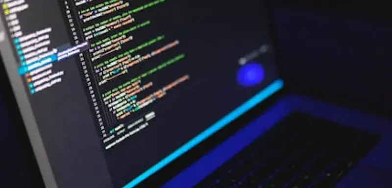 Un ordinateur portable affichant du code coloré dans un environnement sombre, illustration du développement technologique