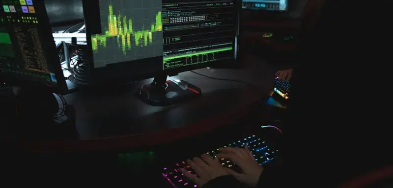Un expert en cybersécurité travaille dans une pièce sombre, tapant sur un clavier coloré avec plusieurs écrans affichant des données