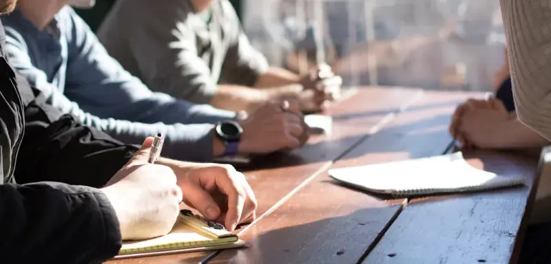 Personnes assises à une table tenant des stylos lors d'une réunion de travail