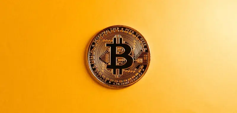 Gros plan sur une pièce de Bitcoin posée sur un fond jaune vif, symbolisant la monnaie numérique