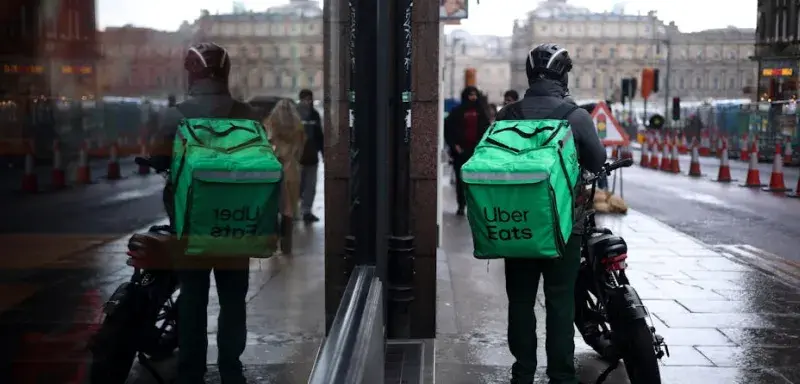 Livreur Uber Eats à moto dans une rue pluvieuse d'Édimbourg avec reflet dans le rétroviseur