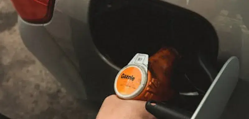 Close-up of a hand refilling a car at a gas station during daylight.