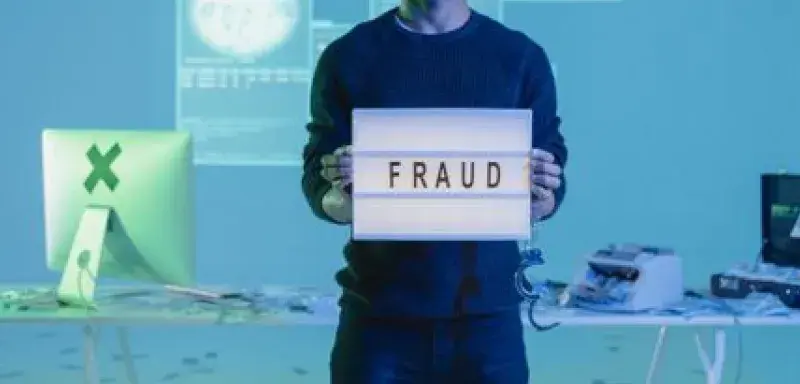 Young man holding a 'fraud' sign in a tech-focused setting with digital and cash elements.