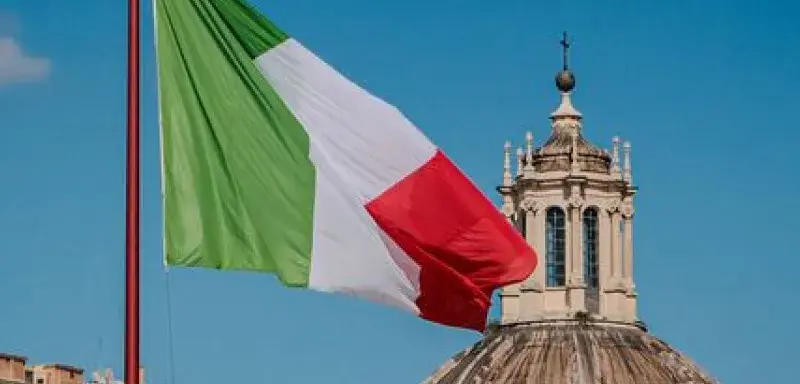 Captivating view of the Italian flag against Roman architecture and blue sky.