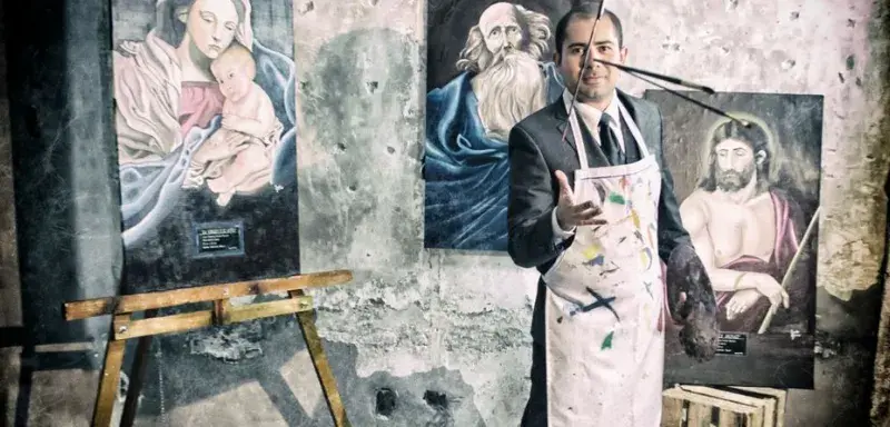 Artist in a suit and apron poses with Renaissance-style paintings in an old studio.