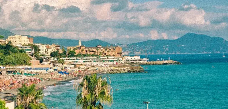 Crowded beach with blue umbrellas and palm trees.