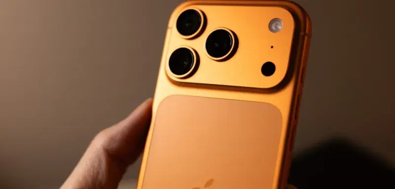 Orange smartphone with triple camera system held.