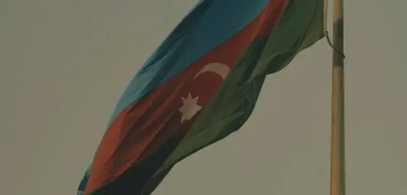 The Azerbaijani national flag waving on a flagpole against a clear sky, symbolizing national pride.