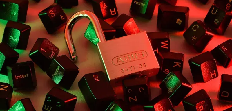 An open padlock surrounded by scattered black computer keyboard keys under red and green light