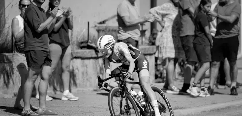 Black and white photo of a female cyclist racing in Lausanne, Switzerland with cheering spectators.