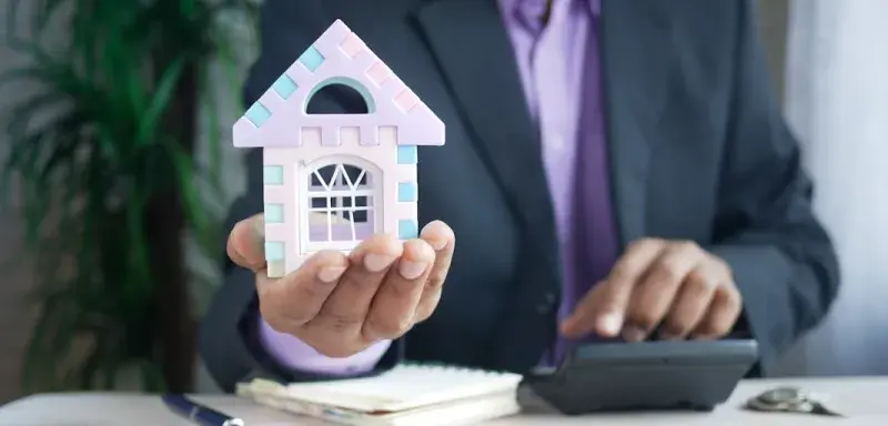 man holding model house at desk with calculator
