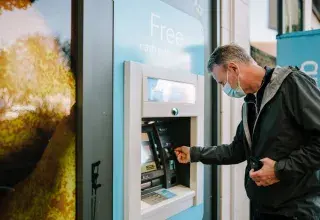 Un homme portant un masque utilise un distributeur automatique de billets en extérieur