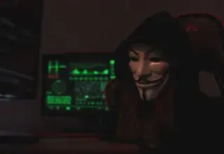 Personne anonyme portant un masque Guy Fawkes travaillant sur un ordinateur dans une pièce sombre, évoquant des activités cybernétiques