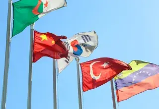 Five national flags from different countries waving on flagpoles under a clear blue sky