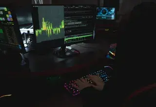 Un expert en cybersécurité travaille dans une pièce sombre, tapant sur un clavier coloré avec plusieurs écrans affichant des données