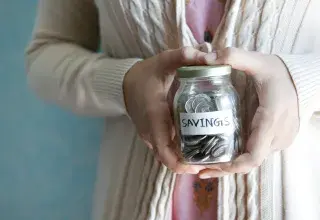 a woman holding a jar with savings written on it
