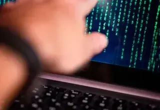 A person points at a glowing code on a computer screen, symbolizing technology interaction.