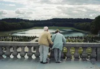 Elderly couple holding hands overlooking a formal garden.