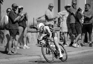 Black and white photo of a female cyclist racing in Lausanne, Switzerland with cheering spectators.