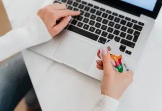 Close-up of a person using a laptop and holding a credit card for online shopping.