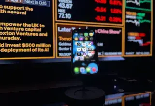 Smartphone displaying AI apps in front of a financial data screen in London.